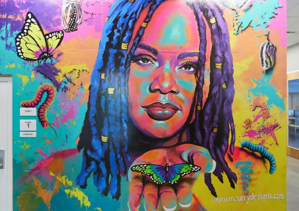 A vibrant mural features a person holding a butterfly with colorful elements like caterpillars and butterflies surrounding them.