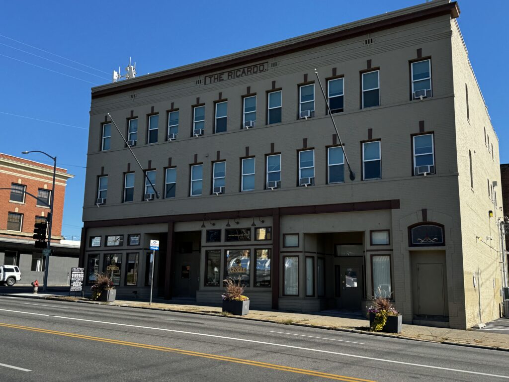 A three-story building called "The Ricardo" with businesses on the ground floor, located on a street corner.