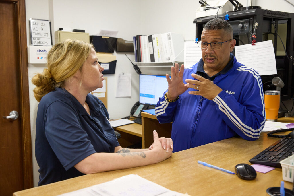 Two people are having a discussion at a desk in an office setting.