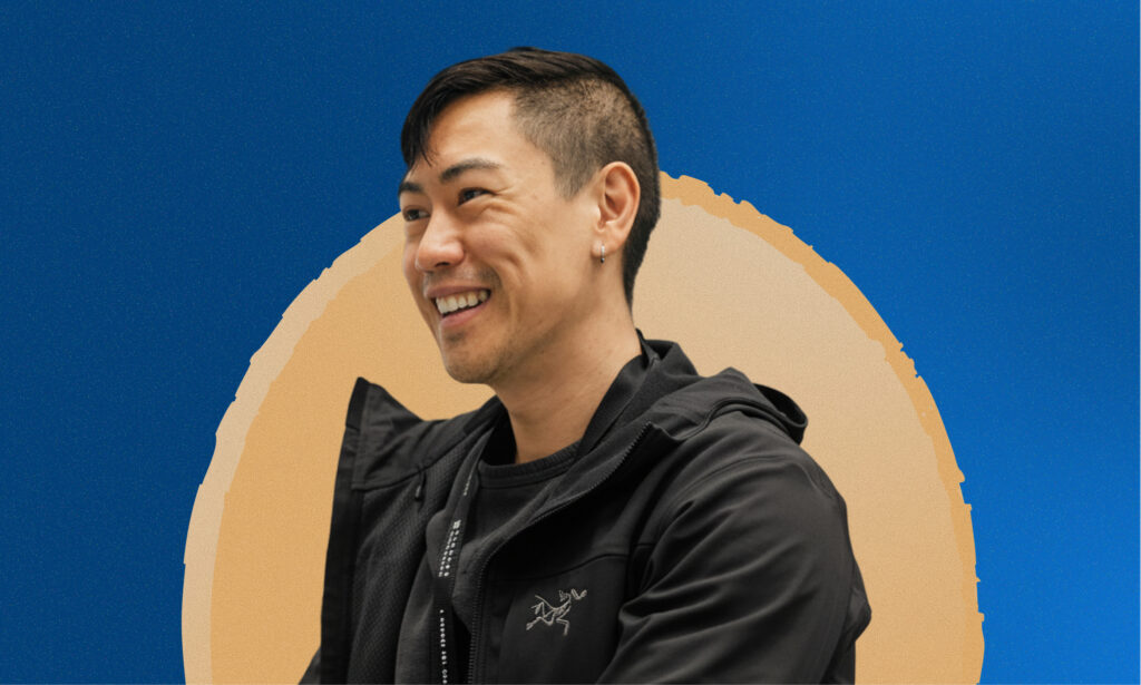 Man smiling with orange circle and blue background behind him.